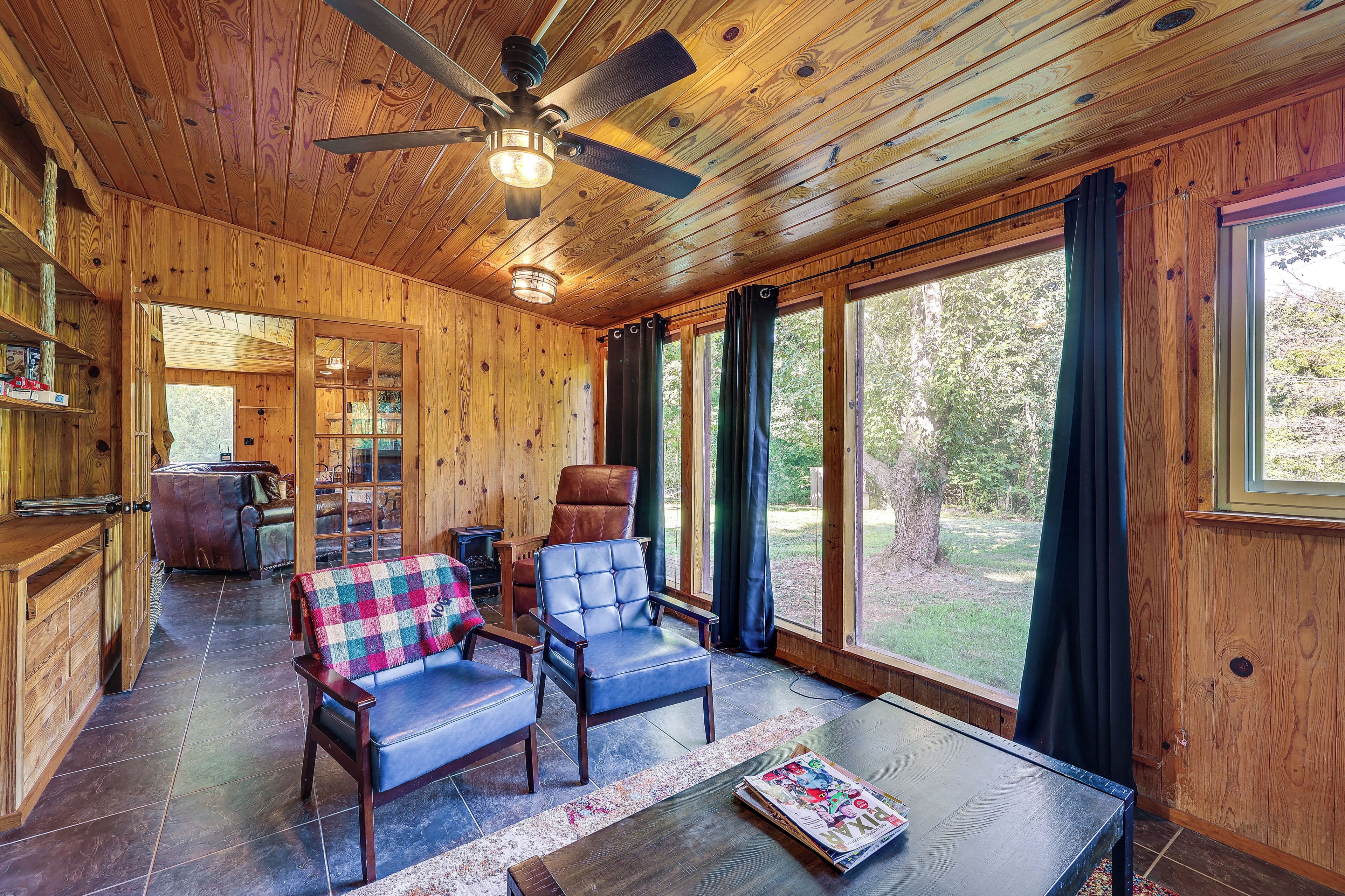 A wooden cabin interior with a ceiling fan, a sofa, a chair, and a table with a magazine.