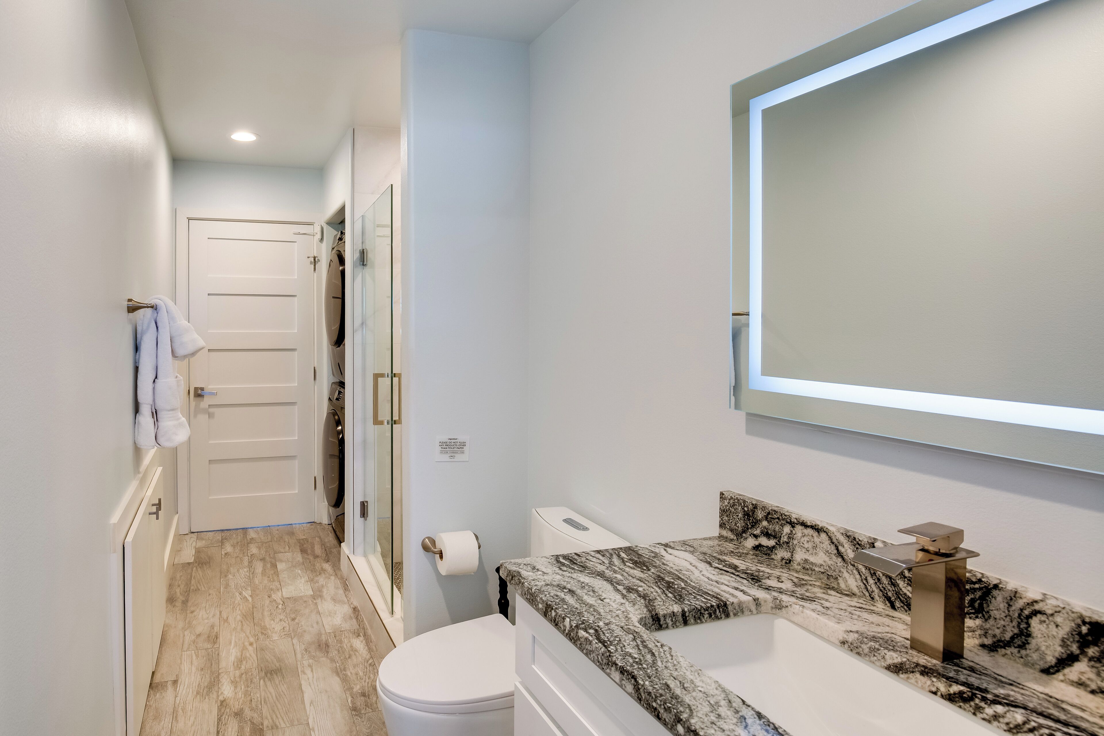 A modern bathroom with a marble countertop, a large mirror, and a toilet.