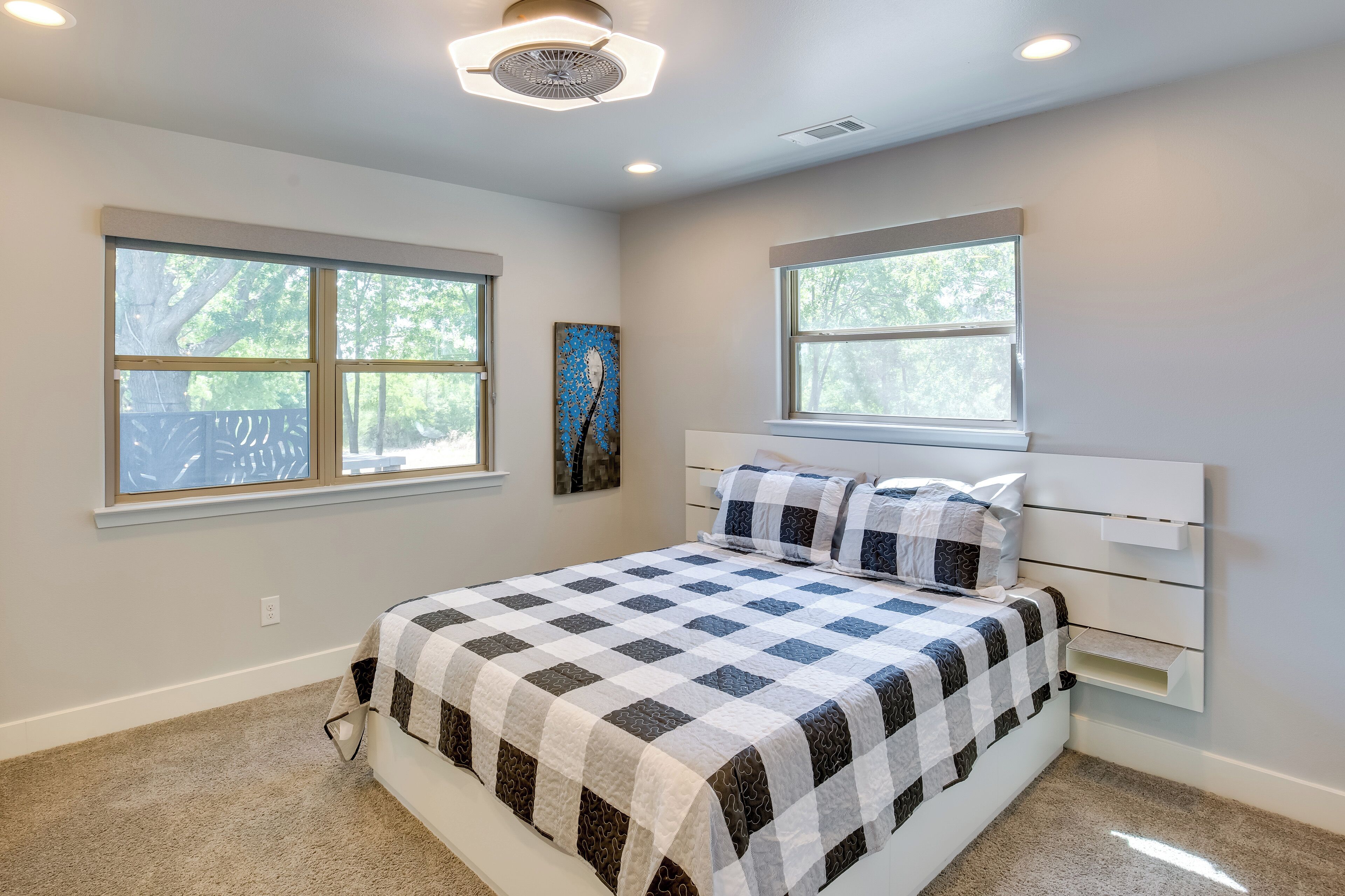 A bedroom with a bed, two windows, a ceiling fan, and a wall-mounted shelf.