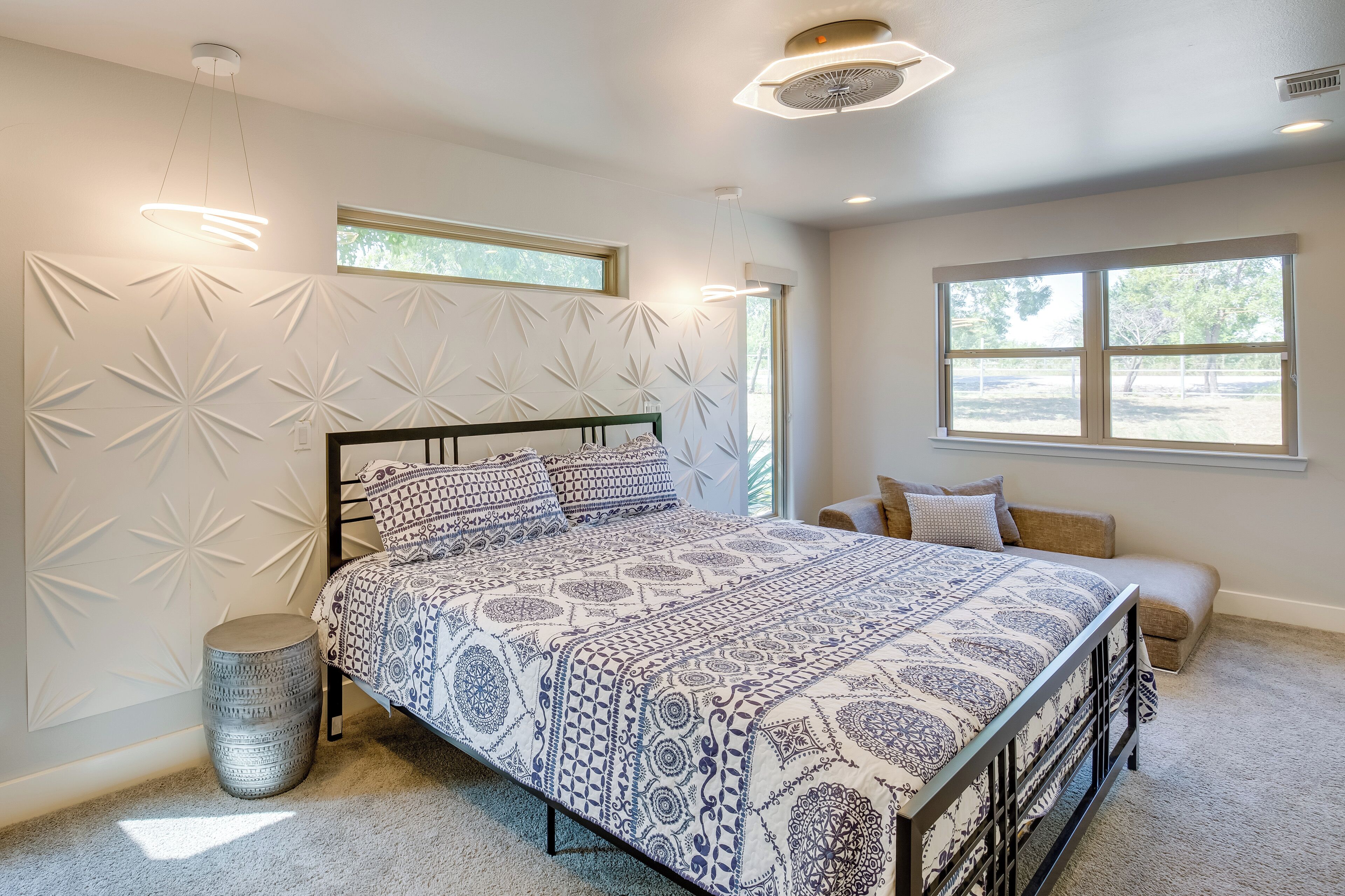 Een slaapkamer met een bed, een rond bijzettafeltje, een raam en een muur met een geometrisch patroon.