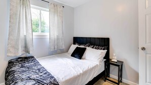 Un dormitorio con cama, ventana con cortinas, mesita de noche y una puerta.
