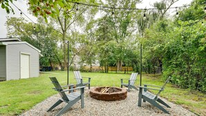 Un patio trasero con un pozo de fuego, cuatro sillas Adirondack y una guirnalda de luces.