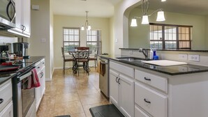 A modern kitchen with white cabinets, a black countertop, and a dining area with a table and chairs. - ~ 10 Mi to Dtwn Mckinney: Home w/ Patio & Yard (McKinney)