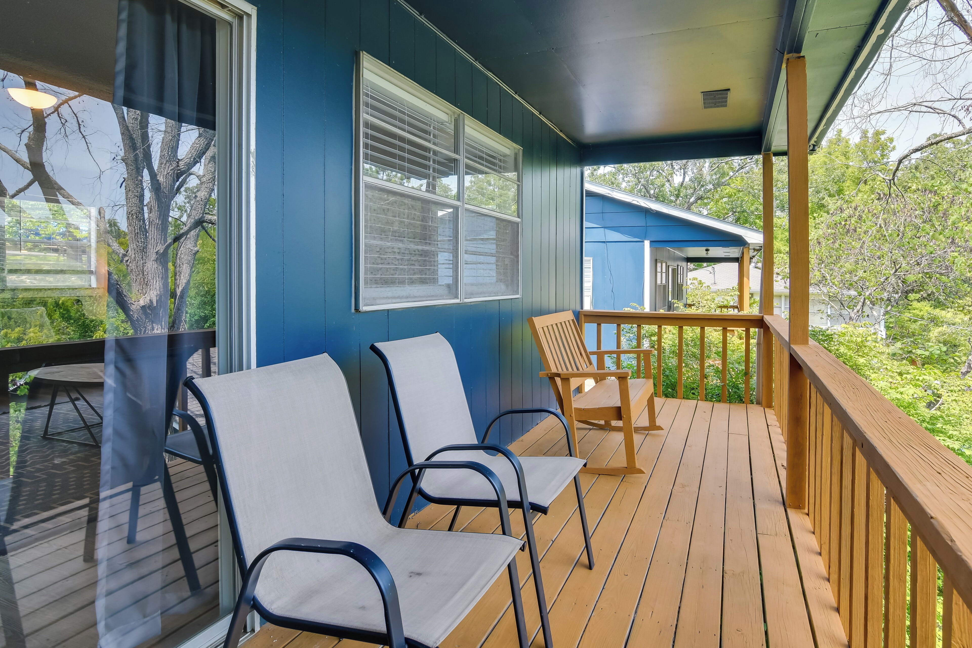 A covered porch with wooden flooring, two white chairs, and a wooden chair.