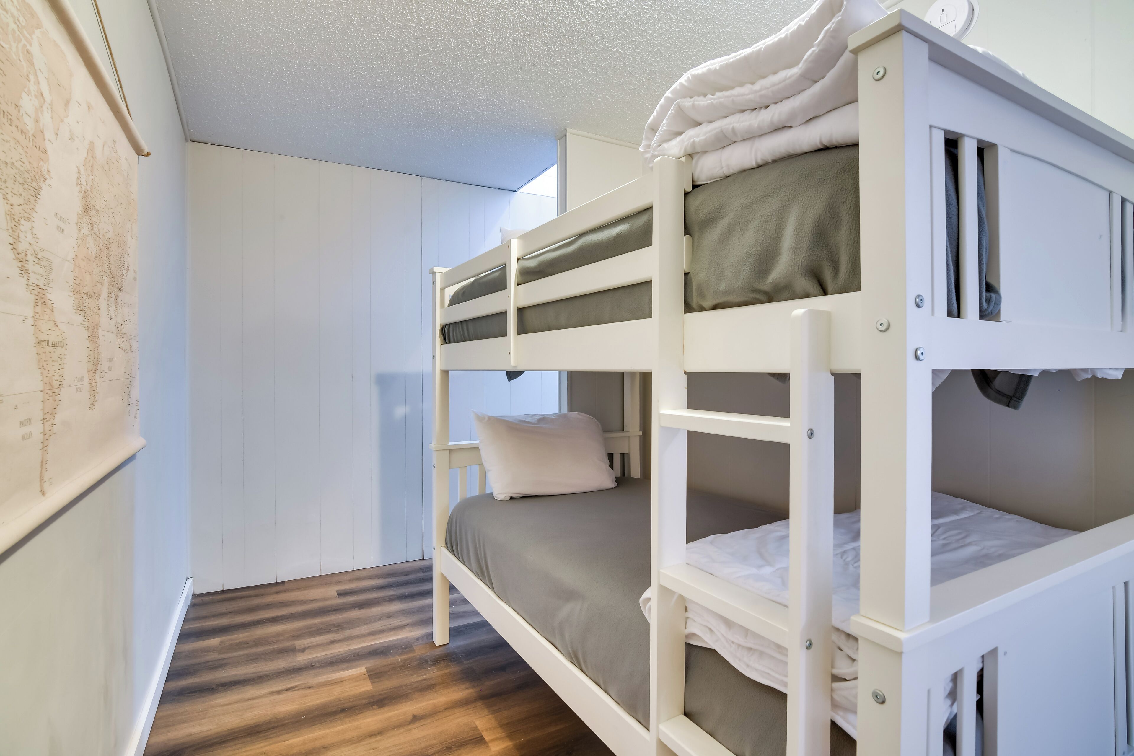 Een slaapkamer met stapelbedden, een houten vloer, witte wanden en een kaart aan de linkerkant.