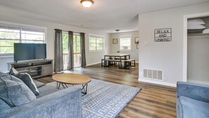 Una sala de estar moderna con sofá, mesa de centro y televisor. Hay una zona de comedor con mesa y sillas, y un cartel que dice “RELAX AND UNWIND”.
