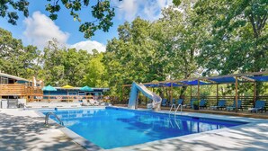 A swimming pool with a slide, lounge chairs, and a wooden deck.