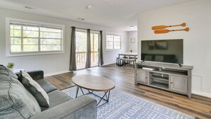 A spacious living room with a grey sofa, a round coffee table, and a flat-screen TV on a wooden stand.
