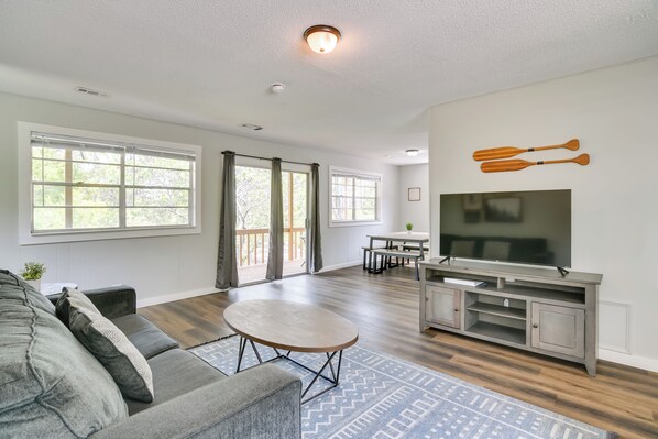 A spacious living room with a grey sofa, a round coffee table, and a flat-screen TV on a wooden stand.