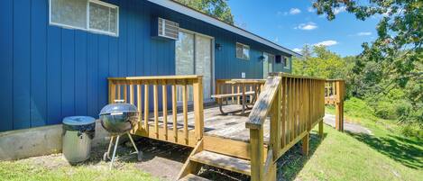A blue mobile home with a wooden deck, a barbecue grill, and a trash can.