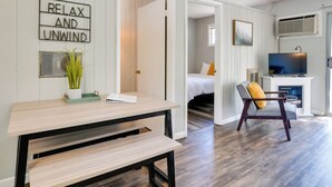 A room with a wooden floor, a bed with a yellow pillow, a TV, and a sign that says "RELAX AND UNWIND". - Kimberling City Oasis: Boat Slip, Kayaks & More! (Kimberling City)