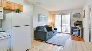 A compact kitchen with a refrigerator, stove, and a small dining table. A gray sofa with cushions is placed near a sliding glass door leading to a balcony. - Kimberling City Home: Boat Slip & Lakefront Bliss! (Kimberling City)