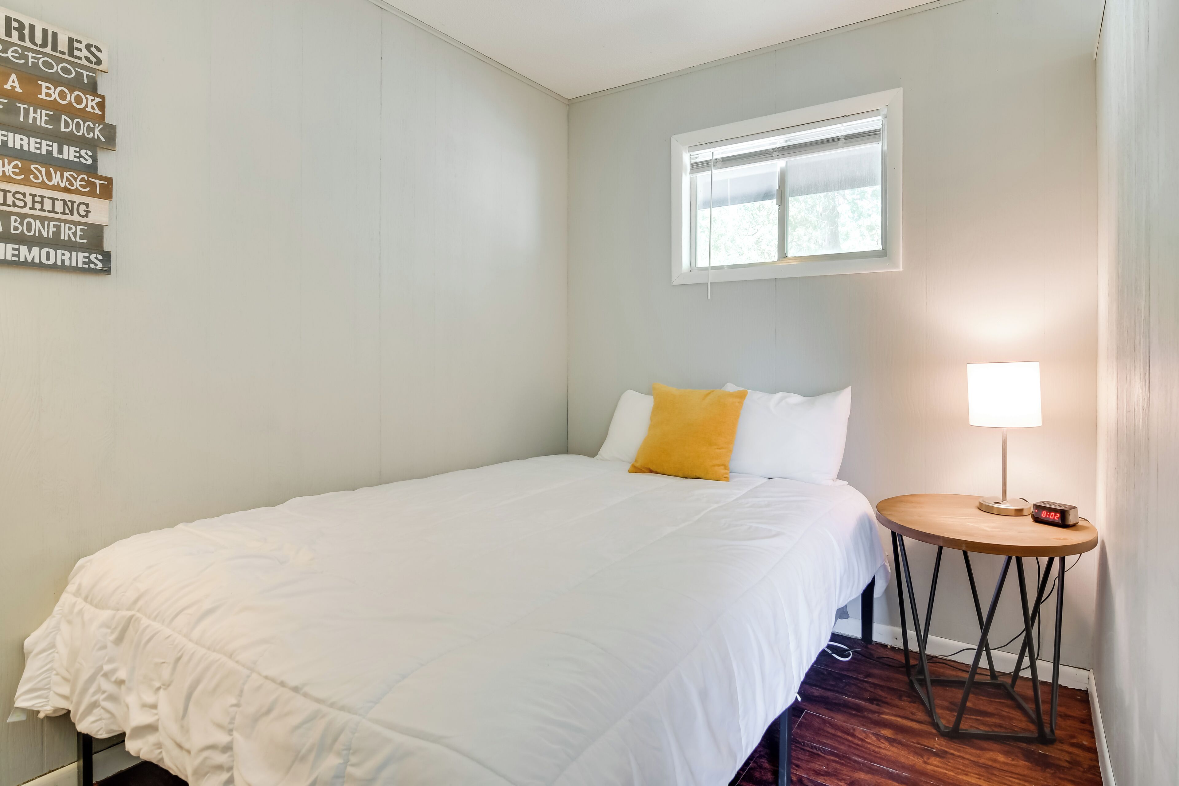 A neatly made bed with white and yellow bedding, a small bedside table with a lamp, and a window with blinds.
