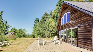 A wooden deck with Adirondack chairs and a picnic table, overlooking a forested area.
