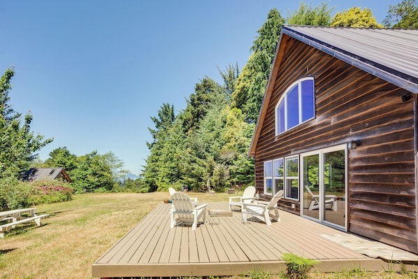 A wooden deck with Adirondack chairs and a picnic table, overlooking a forested area.