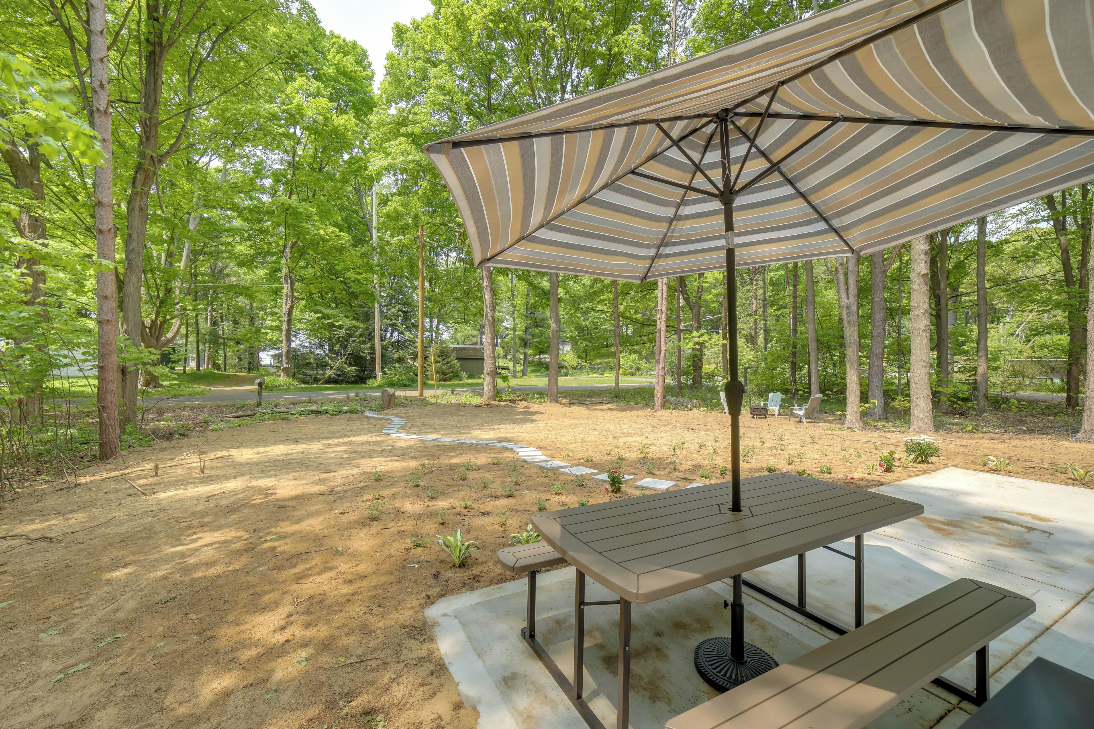 A covered outdoor seating area with a picnic table and benches, surrounded by a forested landscape.