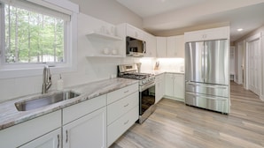 A modern kitchen with white cabinetry, stainless steel appliances, and a large window providing natural light. - Holland Home w/ Fire Pit: Walk to Lake Michigan! (Holland)