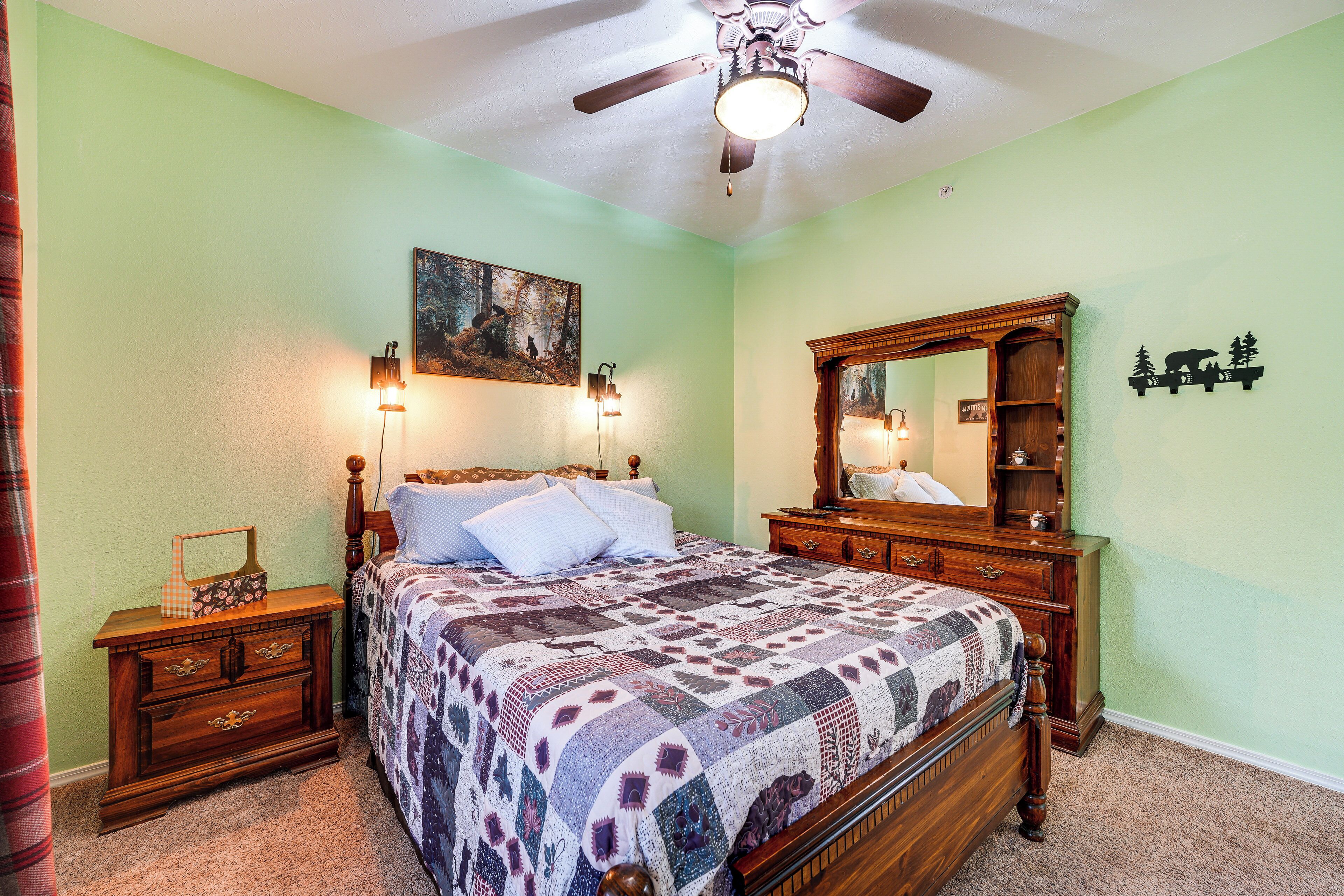 A bedroom with a wooden bed, a nightstand, a dresser, a ceiling fan, and a painting on the wall.