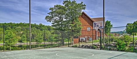An outdoor basketball court with a fence, trees, and a building in the background.
