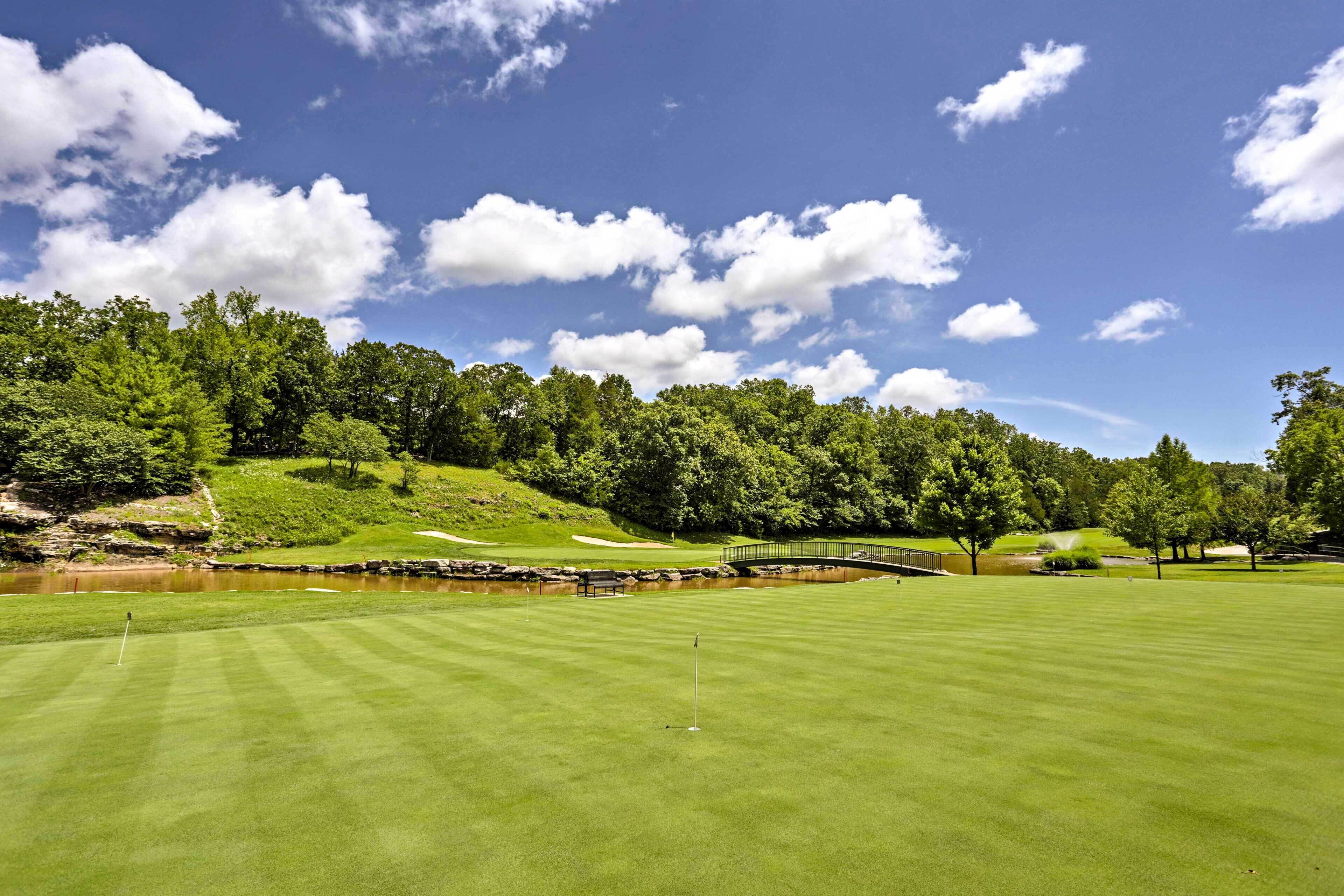 Un campo de golf con cielo despejado, un estanque y un puente.