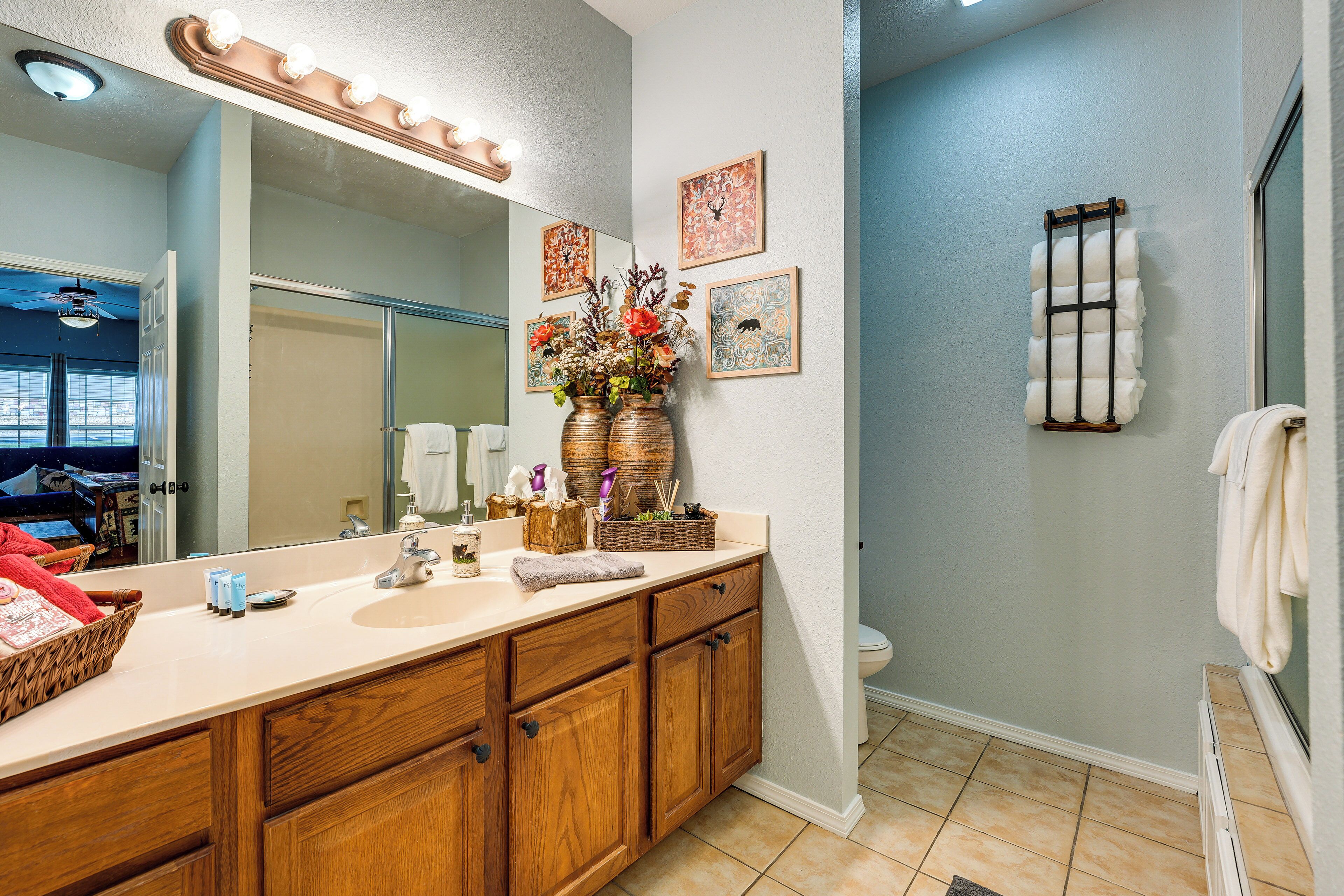A bathroom with a large mirror, vanity, wooden cabinets, and a towel rack.
