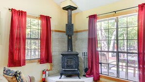 A cozy room with a wood-burning stove, large windows with red curtains, a fire extinguisher, and a fire poker on the windowsill. - Pools & Ski Access: Lackawaxen Cottage w/ Deck! (Lackawaxen)