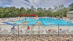 A swimming pool with multiple lanes, surrounded by lounge chairs and umbrellas, with a fence in the foreground and trees in the background. - Pools & Ski Access: Lackawaxen Cottage w/ Deck! (Lackawaxen)