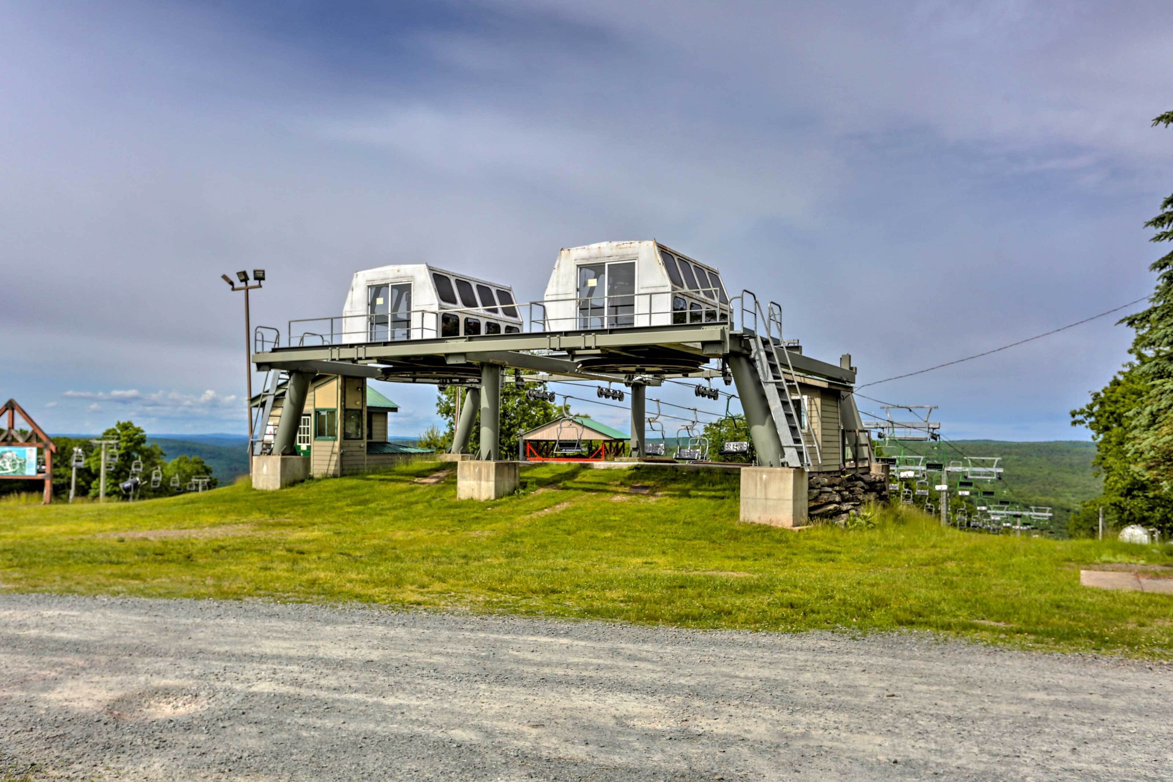 A cable car system with a small building at the base, set against a backdrop of green hills and a cloudy sky.