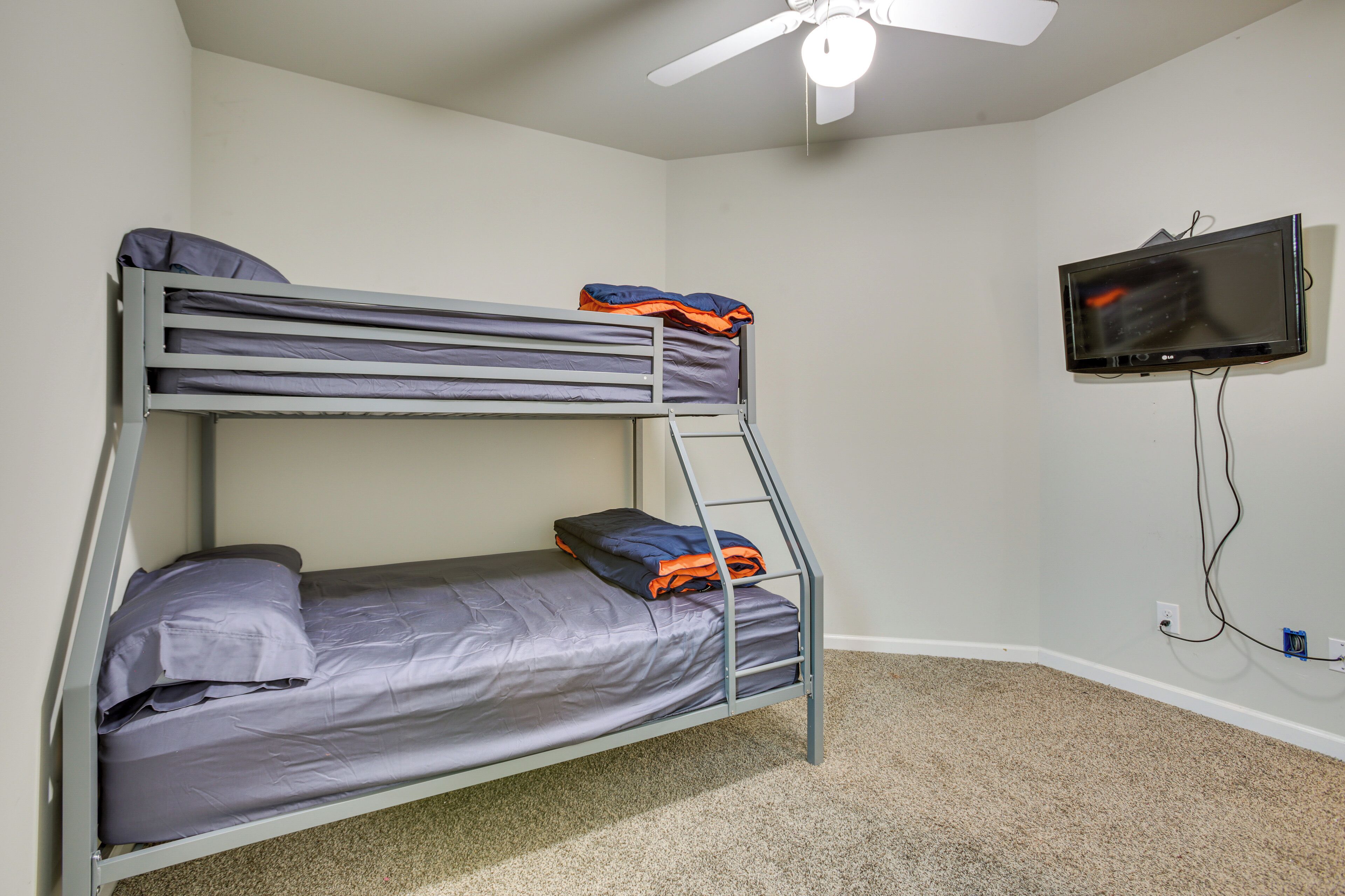 A bunk bed with grey bedding, a ceiling fan, and a TV mounted on the wall.