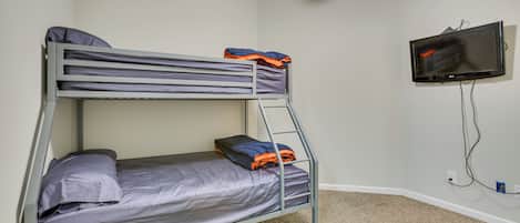 A bunk bed with grey bedding, a ceiling fan, and a TV mounted on the wall.