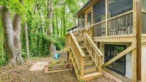 A wooden cabin with a deck and stairs, surrounded by dense forest. - Charming Cary Home ~ 10 Mi to Downtown Raleigh! (Cary)
