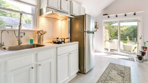 A modern kitchen with white cabinets, stainless steel appliances, and a large window overlooking a patio area. - All-season Vernon Township Lake House Retreat! (Highland Lakes)