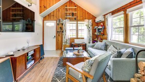 A cozy loft-style living room with a wooden ceiling, a glass coffee table, a sofa, and a bookshelf. - All-season Vernon Township Lake House Retreat! (Highland Lakes)
