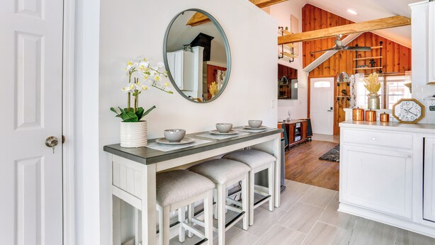 A modern kitchen with white cabinetry, a central island with stools, a large mirror, and a wooden ceiling beam. - All-season Vernon Township Lake House Retreat! (Highland Lakes)
