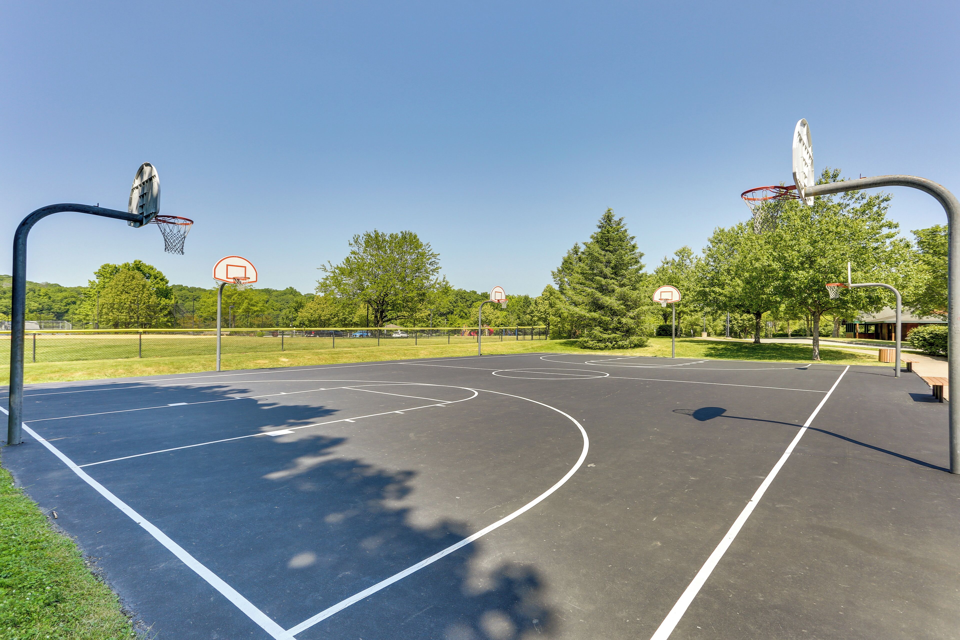 Un terrain de basket en plein air, doté de plusieurs paniers, entouré d’arbres et surplombé d’un ciel dégagé.