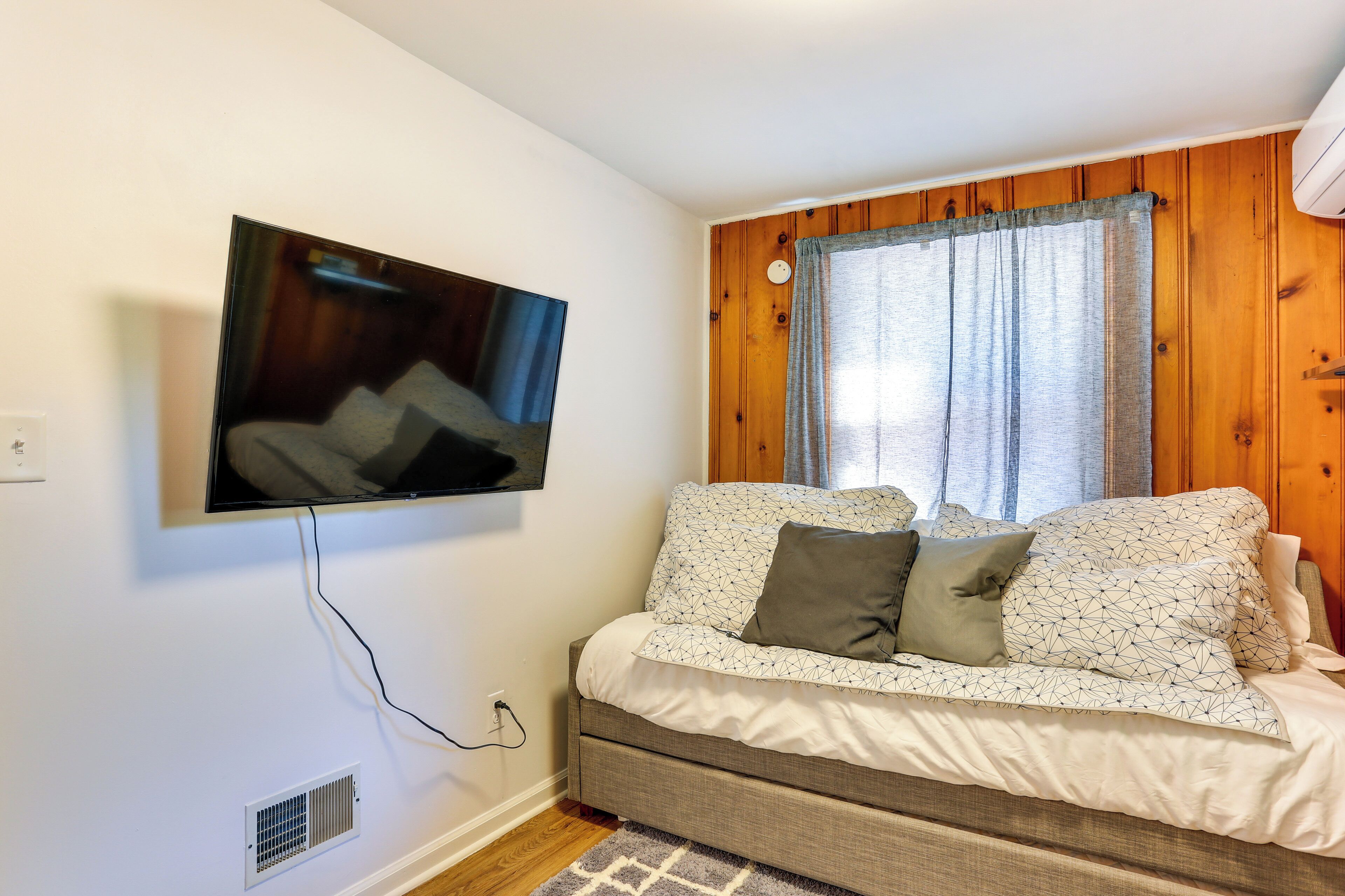 A cozy room with a sofa, a television mounted on the wall, and a window with curtains.