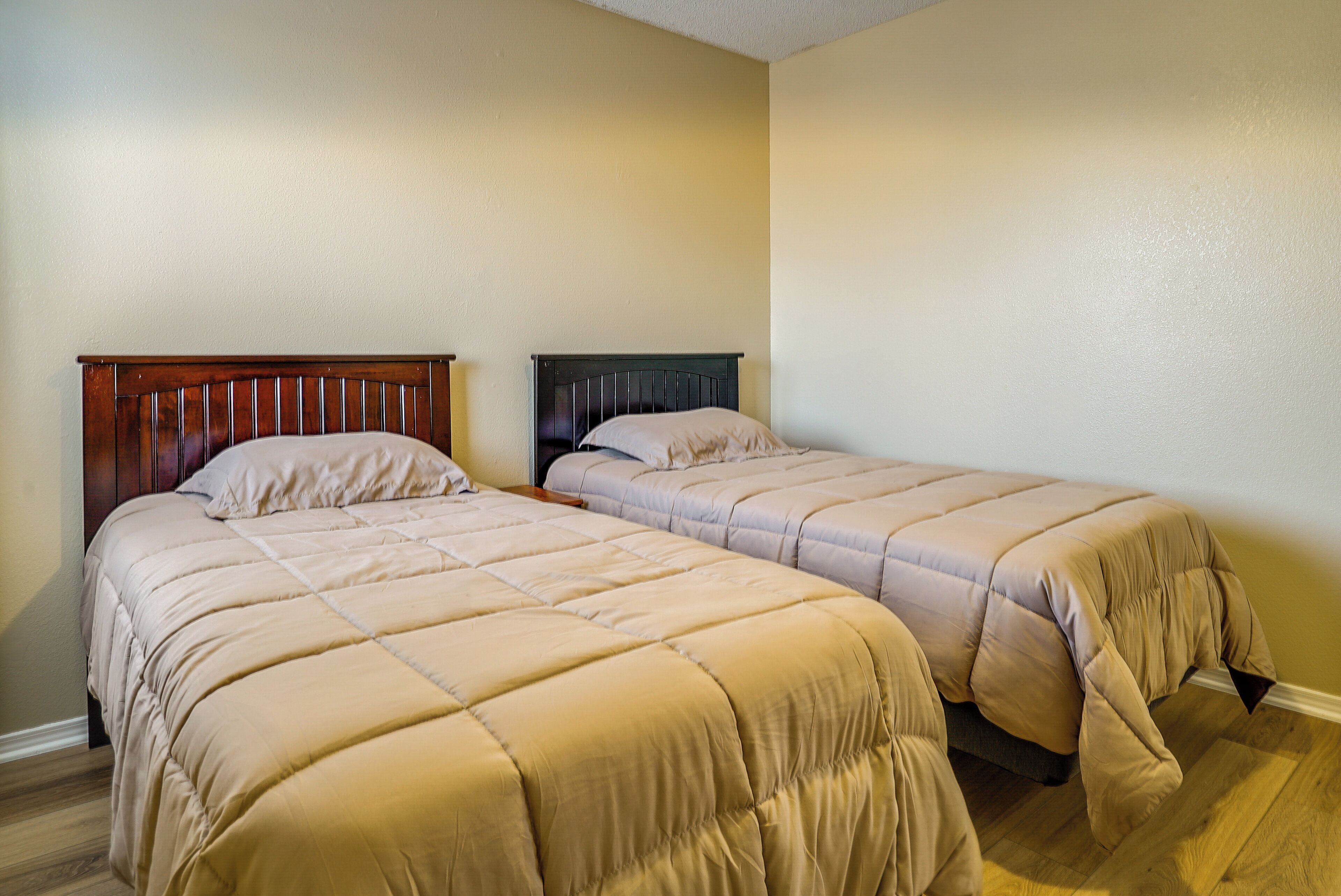 Ein Schlafzimmer mit zwei Einzelbetten, Holz-Kopfteilen und beiger Bettwäsche.