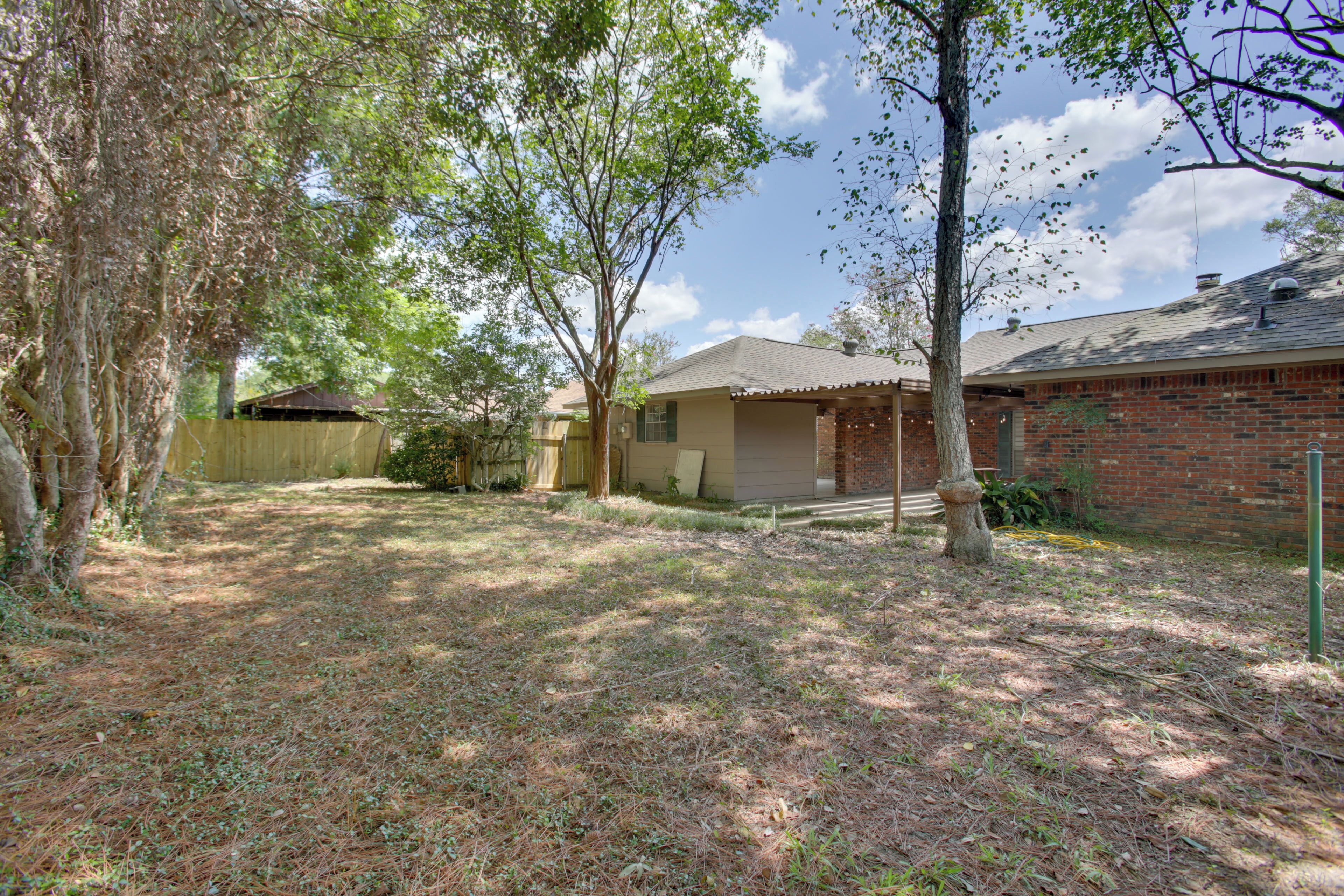 A residential property with a brick house, a covered patio, and a yard with trees and grass.