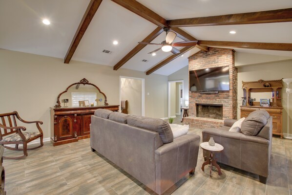 A spacious living room with a fireplace, a ceiling fan, and a wooden dining area.