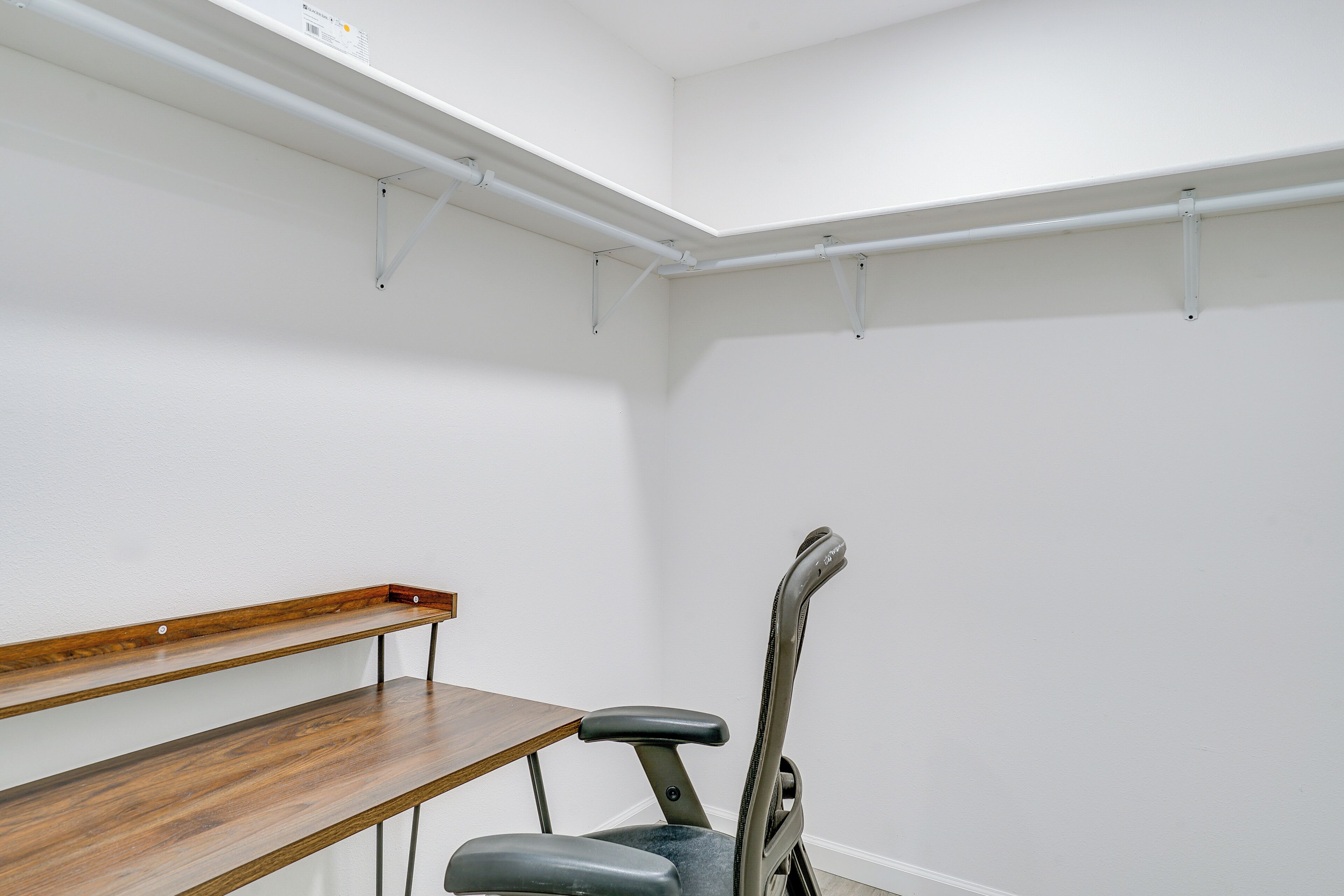 A corner room with white walls, a wooden bench, and a chair.