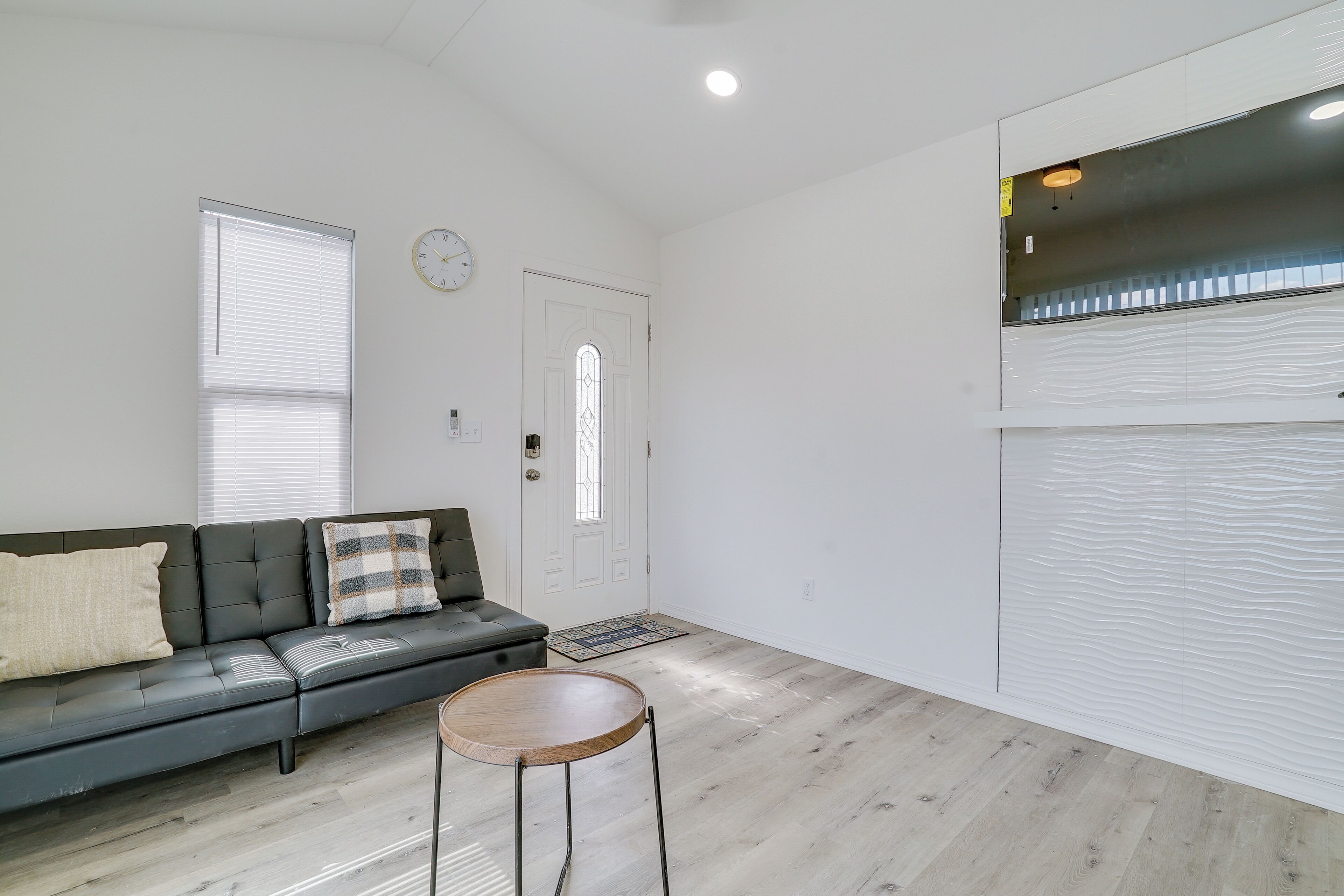 A modern living room with a black leather sofa, a wooden side table, and a white door with a glass window.