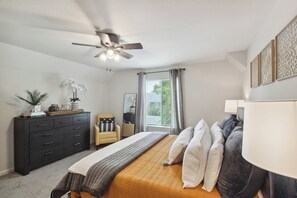 A bedroom with a bed, a ceiling fan, a dresser, a chair, and a window with curtains. - Overland Park Condo, Close to Lakes & Parks! (Overland Park)