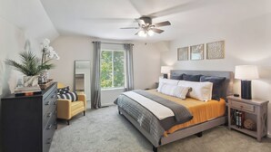 Un dormitorio con cama, cómoda, mesita de noche, ventilador de techo y ventana con cortinas.