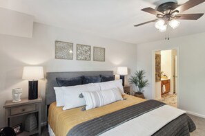 A bedroom with a bed, two bedside lamps, a ceiling fan, and a nightstand with a lamp and decorative items. - Overland Park Condo, Close to Lakes & Parks! (Overland Park)