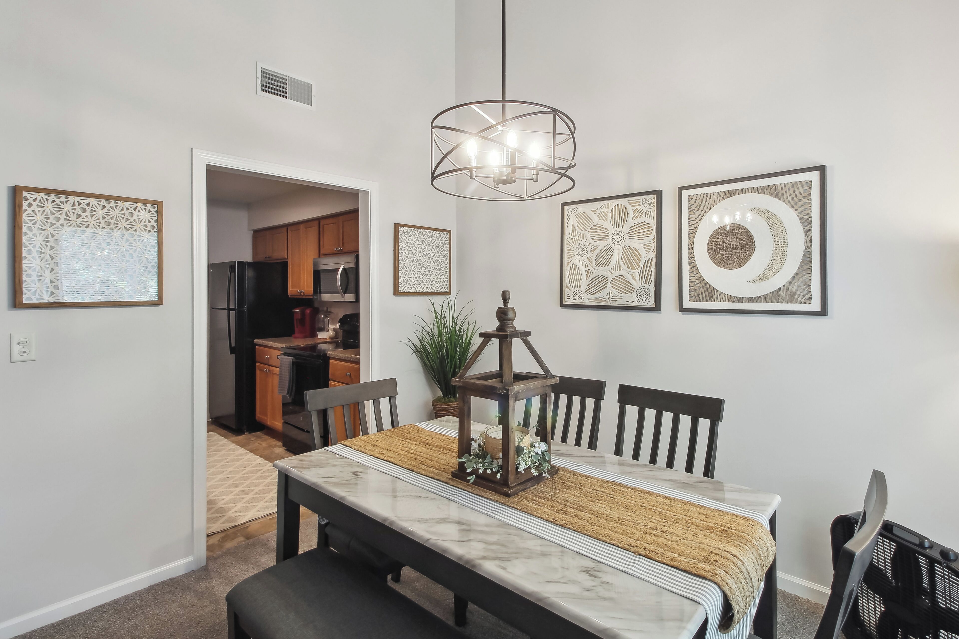 A dining area with a marble table, black chairs, a woven placemat, and a hanging light fixture.