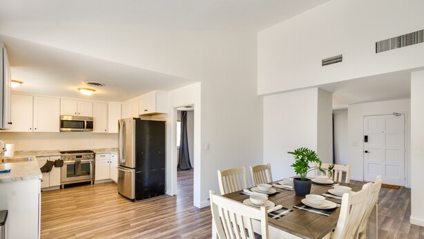 A modern kitchen with white cabinets, stainless steel appliances, and a dining area with a wooden table and white chairs. - Quiet Ridgecrest Vacation Rental w/ Private Yard! (Ridgecrest)