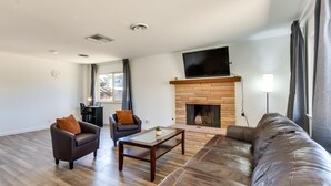 A living room with a leather sofa, two armchairs, a coffee table, a fireplace, and a flat-screen TV mounted above it. - Quiet Ridgecrest Vacation Rental w/ Private Yard! (Ridgecrest)