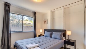 A neatly made bed with a grey duvet, two bedside lamps, and a window with curtains. - Quiet Ridgecrest Vacation Rental w/ Private Yard! (Ridgecrest)