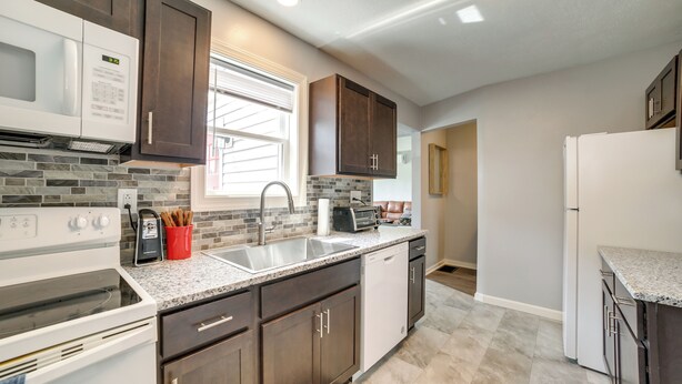 A modern kitchen with dark wood cabinets, a granite countertop, a built-in microwave, and a dishwasher.