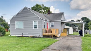 A two-story house with a covered porch, a red door, and a small deck.